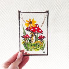 a hand holding up a small card with mushrooms and flowers on it