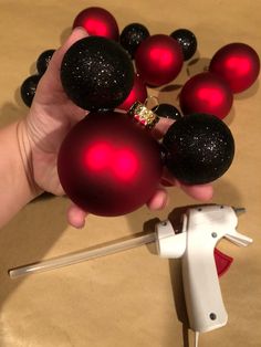 a hand holding red and black ornaments in front of a white sprayer on a table