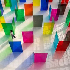 a man is walking among colorful cubes in an art museum, with shadows on the floor