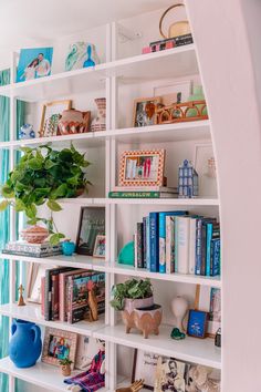 a bookshelf filled with lots of books next to a blue vase and potted plant