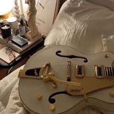 an electric guitar sitting on top of a bed next to a night stand and lamp