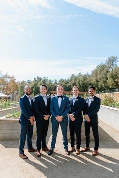 a group of men standing next to each other wearing suits and bow ties in front of trees