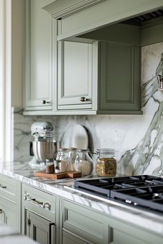 a kitchen with green cabinets and marble counter tops, along with an oven hood over the stove