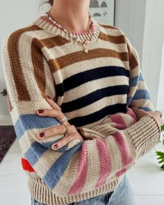 a woman standing with her arms crossed wearing a multicolored striped sweater and jeans