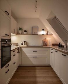 an attic kitchen with white cabinets and wood flooring is lit by the light coming through the window