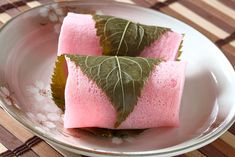 two pieces of pink and green food on a white plate next to a bamboo mat