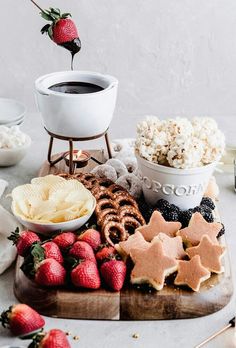 an assortment of snacks are arranged on a wooden platter, including strawberries, pretzels, and popcorn