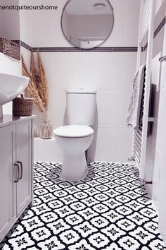 a white toilet sitting next to a sink in a bathroom under a round mirror on the wall