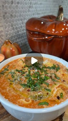 a white bowl filled with soup next to bread and a pumpkin on the table in front of it