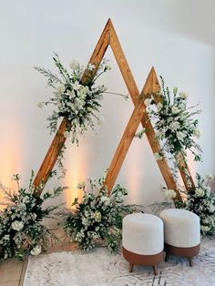 an arrangement of white flowers and greenery on display in front of a wall with wooden frames