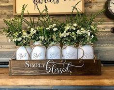 four mason jars with flowers in them are sitting on a wooden shelf next to a clock