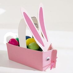 a pink box filled with easter eggs and bunny ears on top of a white table