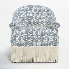 a blue and white patterned chair with fringes on the bottom, in front of a white background