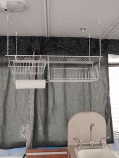 a bathroom with a sink, toilet and hanging basket on the curtained window sill