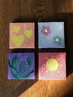 four small square paintings with different designs on them sitting on top of a wooden table