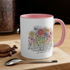 a pink and white coffee mug sitting on top of a wooden table next to a cookie