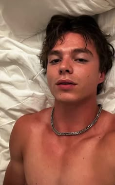 a shirtless young man laying in bed wearing a chain around his neck and chest