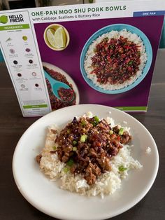 a white plate topped with rice covered in meat and veggies next to a box