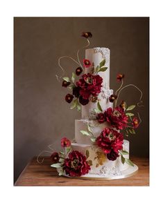 a three tiered wedding cake with red flowers on the top and bottom, sitting on a wooden table