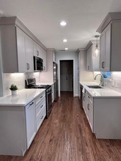 an empty kitchen with white cabinets and wood flooring, along with stainless steel appliances