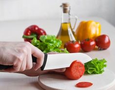 a person holding a knife over a cutting board with tomatoes and lettuce