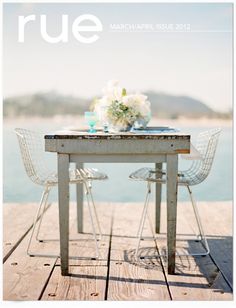 a table and chairs sitting on top of a wooden pier next to the ocean with flowers