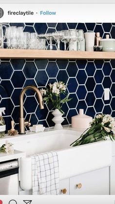 a kitchen with blue tiles and white flowers on the counter top next to a sink