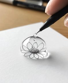 a hand holding a pen writing on top of a piece of paper with a flower in it