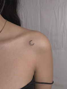 the back of a woman's shoulder with a small crescent tattoo on her left shoulder