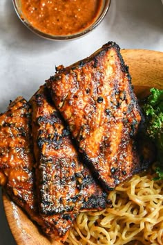 two pieces of grilled meat on top of noodles and broccoli in a bowl