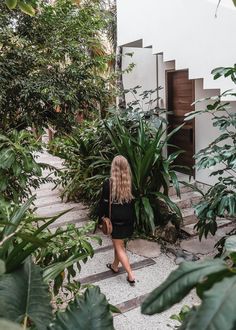 a woman is walking down the steps in front of some trees and plants with her back to the camera