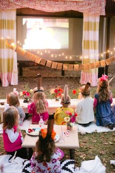 a group of children sitting around a table with food in front of a projector screen