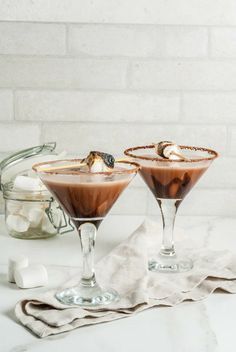 two martini glasses filled with chocolate and marshmallows on a white countertop