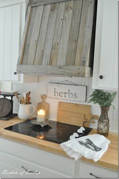 a kitchen with white cabinets and an old wooden oven hood over the stove is filled with utensils