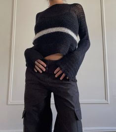 a woman standing in front of a white wall wearing black pants and a cropped sweater