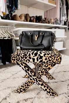 a leopard print stool with a black handbag on it and clothes in the background