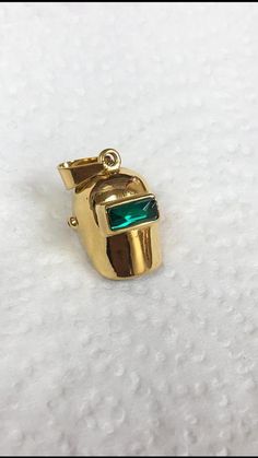 a gold pendant with a green stone in the center on a white surface, close up