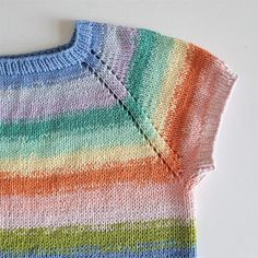 a knitted sweater with multicolored stripes on the front and back, sitting on a white surface