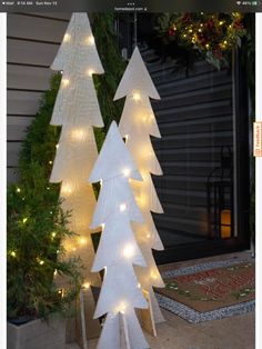 three white christmas trees sitting in front of a house with lights on the top and bottom