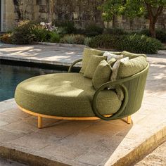 a green chair sitting on top of a stone floor next to a swimming pool with trees in the background