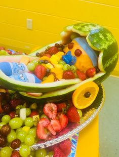 a bowl filled with fruit and vegetables on top of a table next to a yellow wall