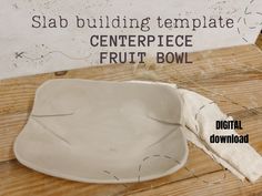 a white bowl sitting on top of a wooden table next to a sign that says, slab building template centerpiece fruit bowl