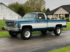 a blue and white pickup truck parked on the side of a road in front of a house