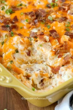 a casserole dish with bacon, cheese and green onions in it on a wooden table