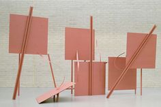 an abstract sculpture made out of pink boxes and sticks with one piece falling off the ground