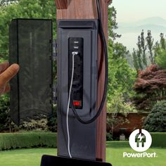 a person is pointing at an electronic device on a wooden pole in front of a green yard