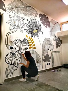 a woman is painting a wall with flowers on it