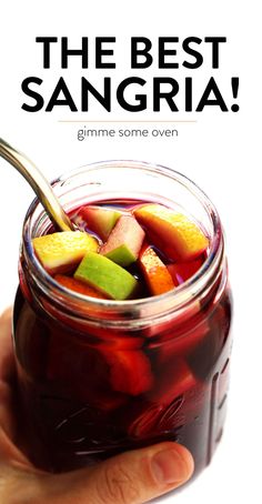 a person holding a spoon in a jar filled with sanggraa and sliced fruit