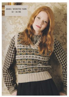 a woman with long red hair wearing a sweater and skirt, standing in front of a wall