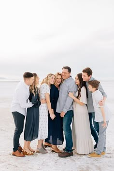 a group of people standing on top of a sandy beach next to the ocean with their arms around each other